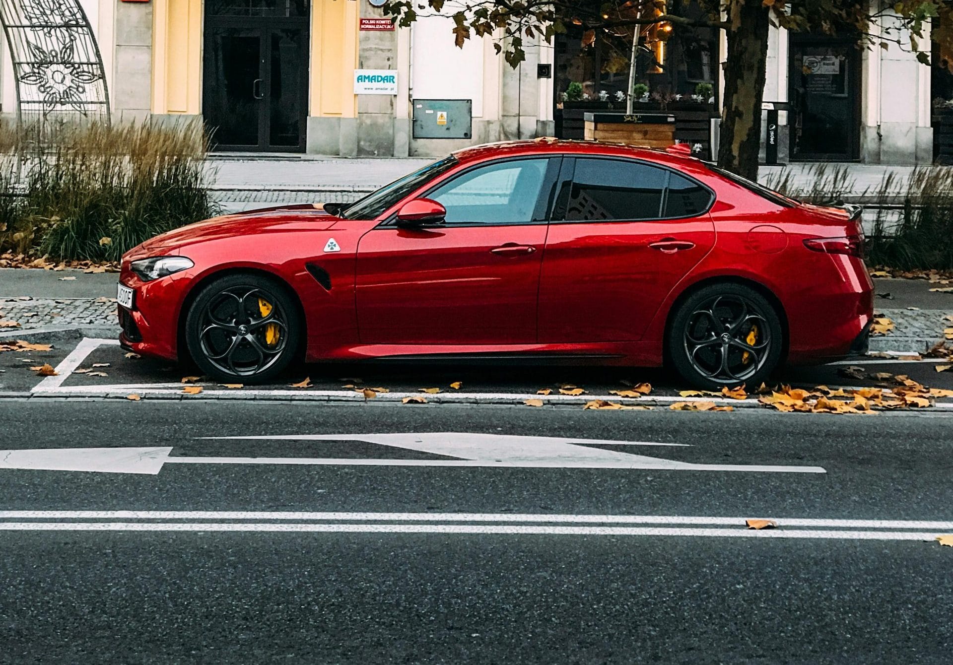 A sleek red sports car parked on a city street lined with autumn trees.